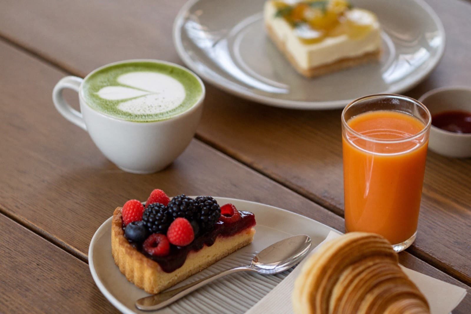 Matcha latte, berry tart and fresh juice on a timber table
