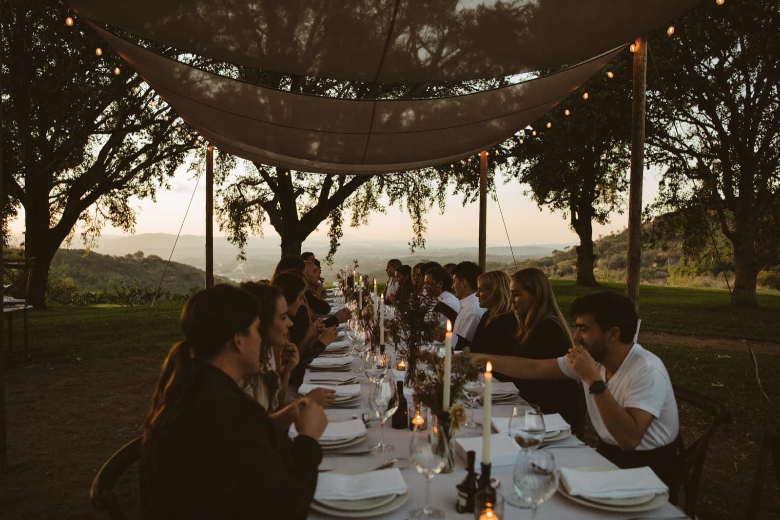 Candlelit banquet table under a canvas pavilion at dusk